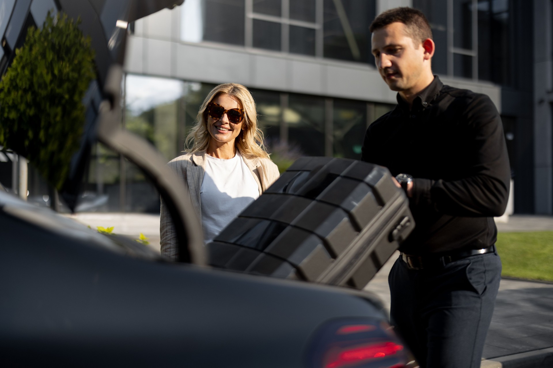Businesswoman waits while chauffeur packs a suitcase in car trunk